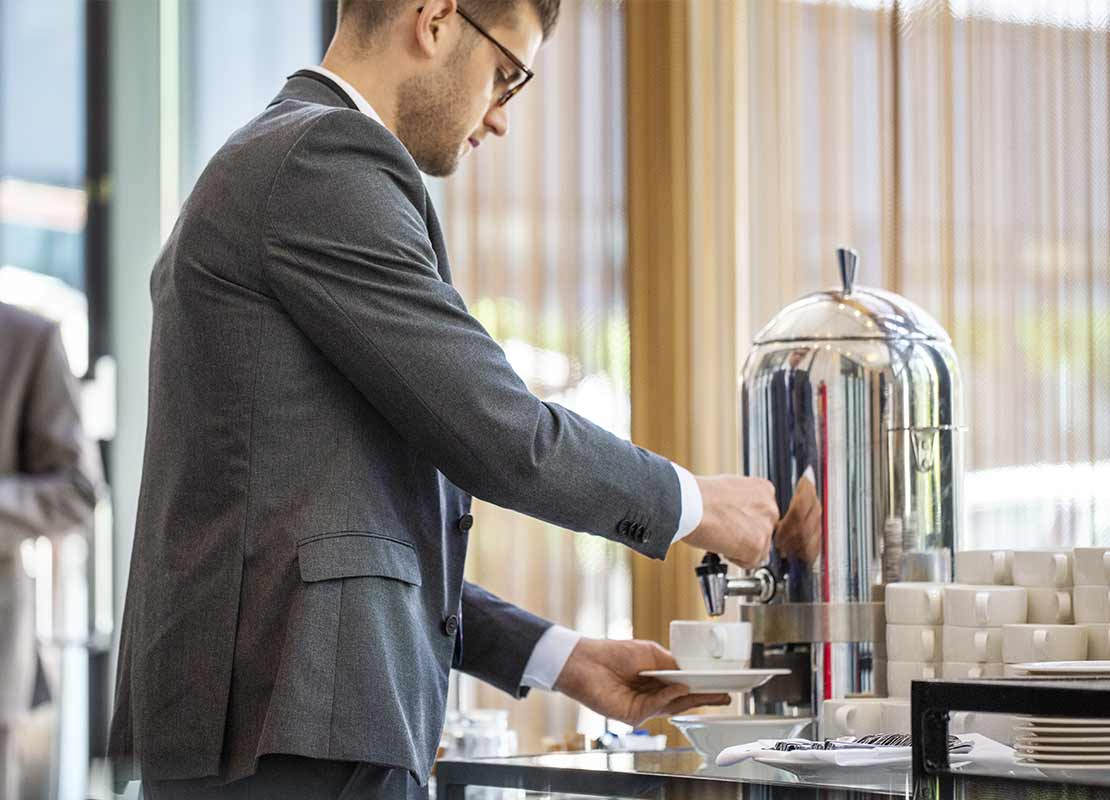 Participante de un evento corporativo sirve un café NESCAFÉ® de una cafetera dispuesta por un servicio de catering